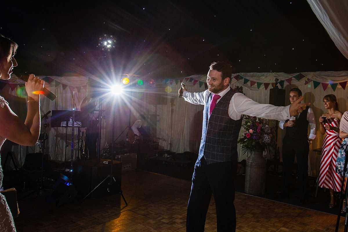 groom with his arms stretched out as he looks adoringly at his wife as she sings to him