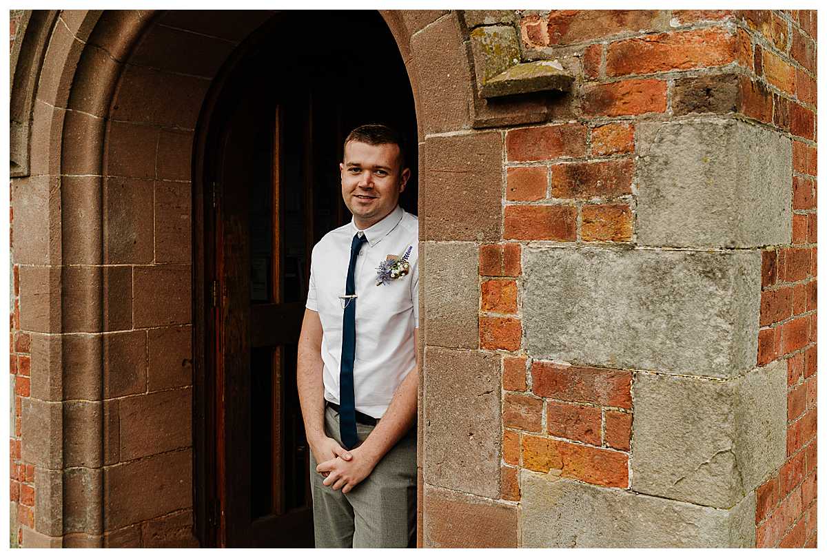 groom looking happy and relaxed in the doorway at marbury church wedding shropshire
