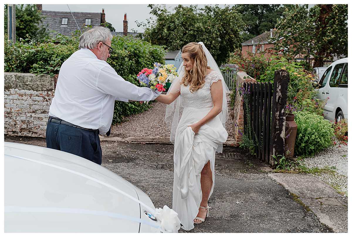 driver handing bride her bouquet as she gets out the car at marbury church shropshire