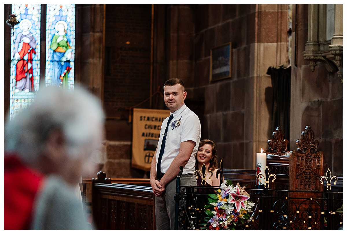 groom watching his bride, smiling, as she walks down the aisle at marbury church shropshire