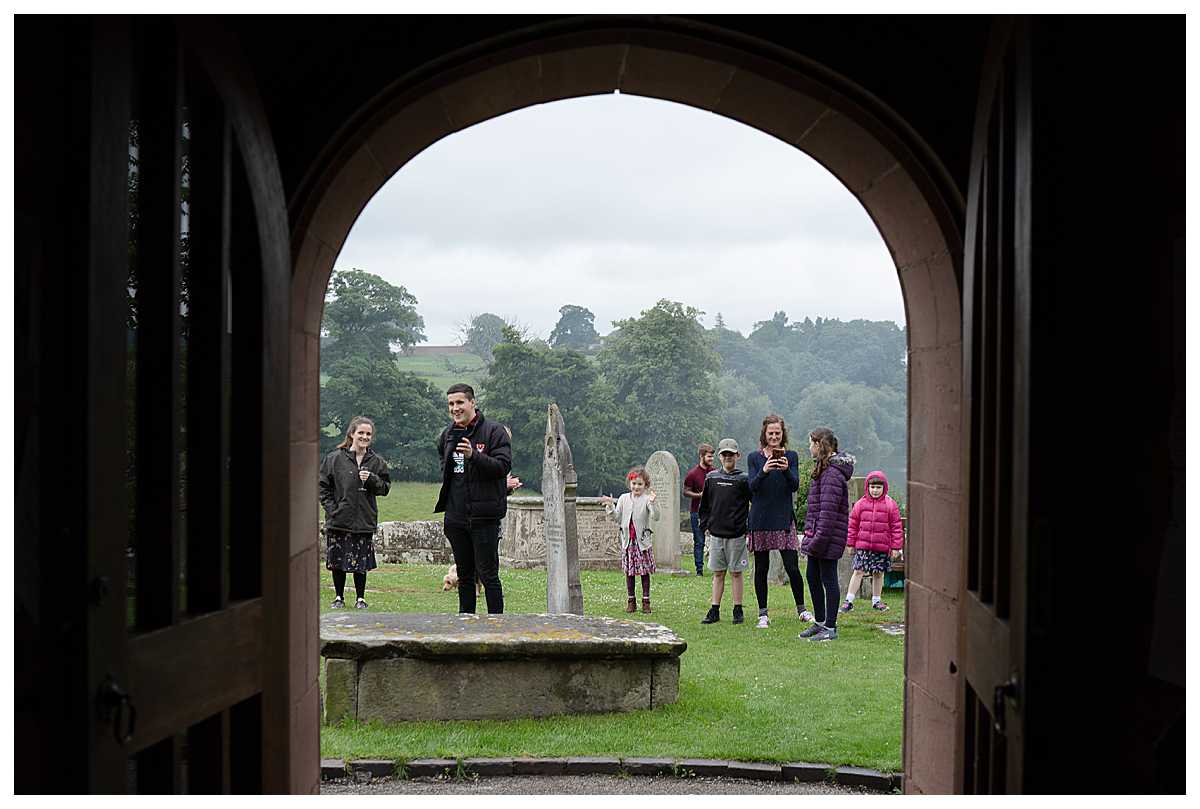 extended family watching the bride and groom walking out of church - excited to see them, shropshire wedding photographer