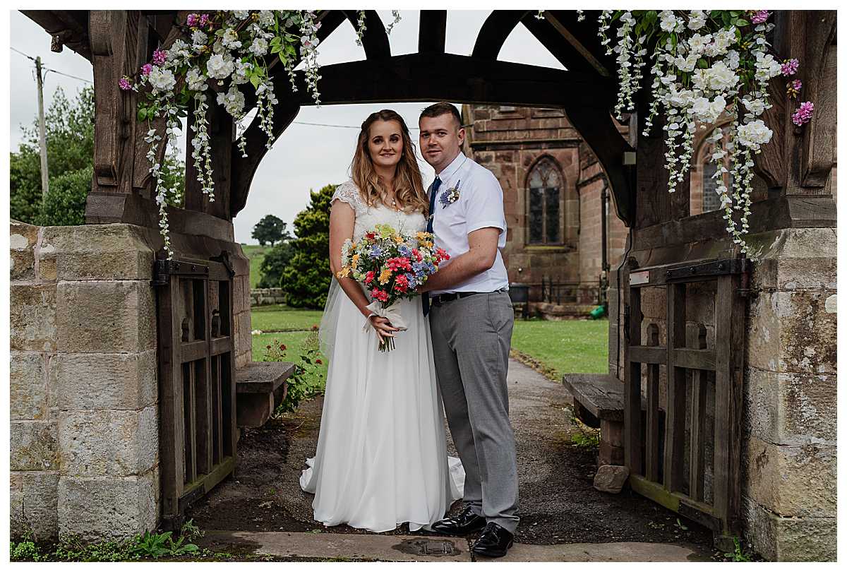 bride and groom under flower arch at marbury church whitchurch shropshire