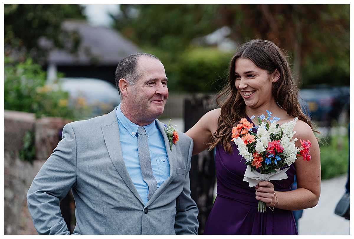 father of the bride emotional and very happy giggling with a bridesmaid outside the church, shropshire wedding photographer