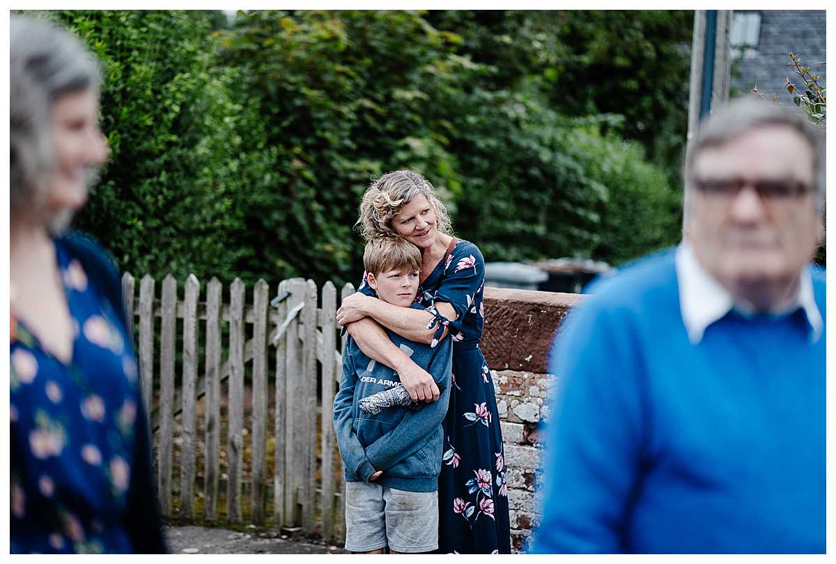 wedding guest cuddling her son outside the church as she people watches - shropshire wedding photographer