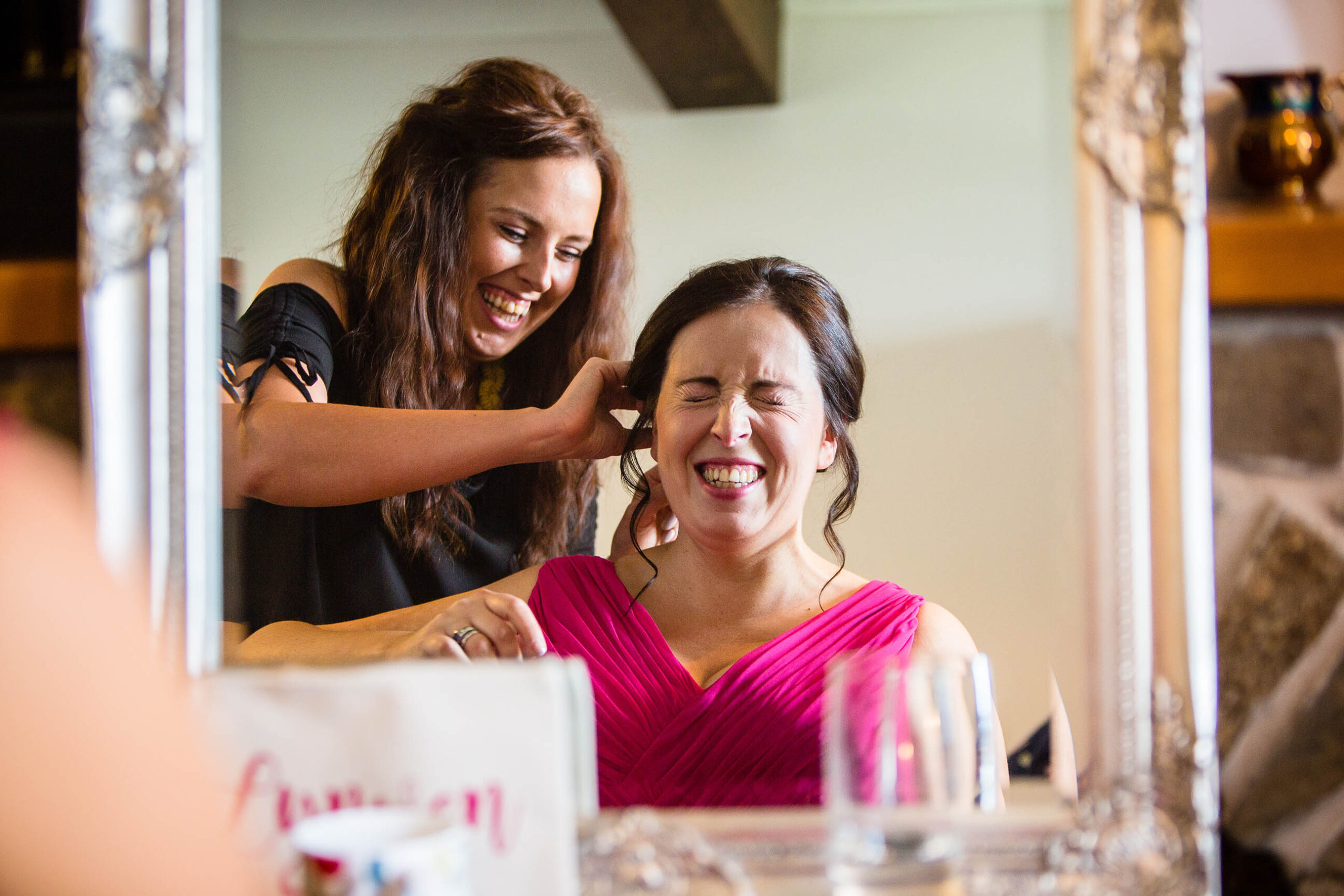 Bridesmaid giggling in the mirror as hair and makeup artist said something funny// welsh wedding photographer