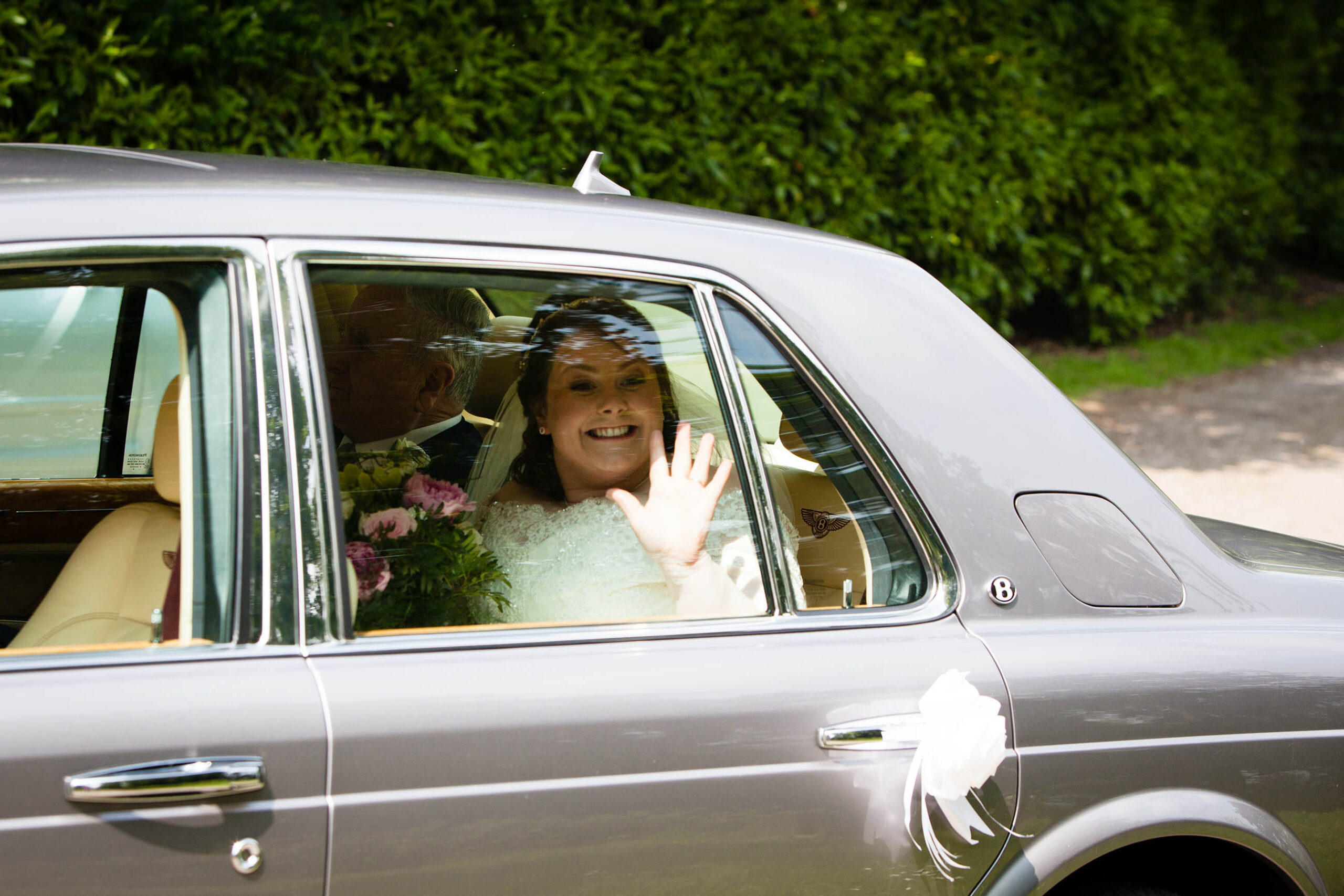 Bride waving excitedly out of the window as she arrives at Bronington Church, Wales Wedding Photographer