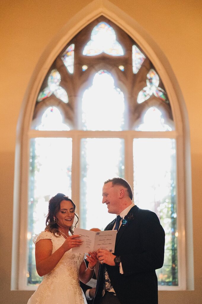 Bride and Groom giggling between themselves as they sing the hymn during their ceremony // Bolton Wedding Photographer