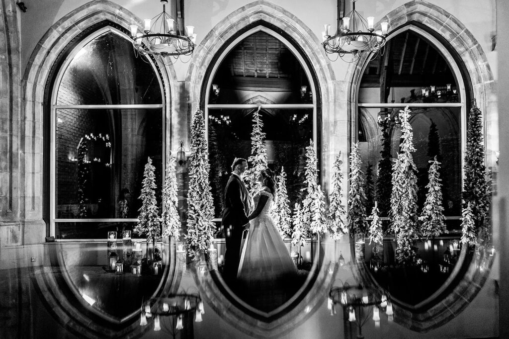 Bride and groom holding hands in the large arch windows at Cloisters, Bolton with a winter
wonderland backdrop