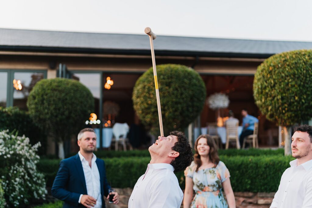 Wedding guest balancing a croquet club on the bridge of his nose infront of wedding guests at Pryers Hayes, near Chester