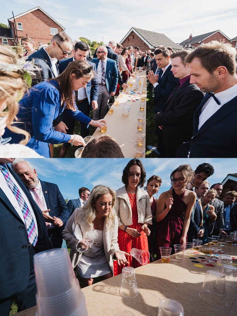 A large group of guests playing "flip the cup" drinking game - two teams set up against long tables in the garden at a Welsh DIY wedding