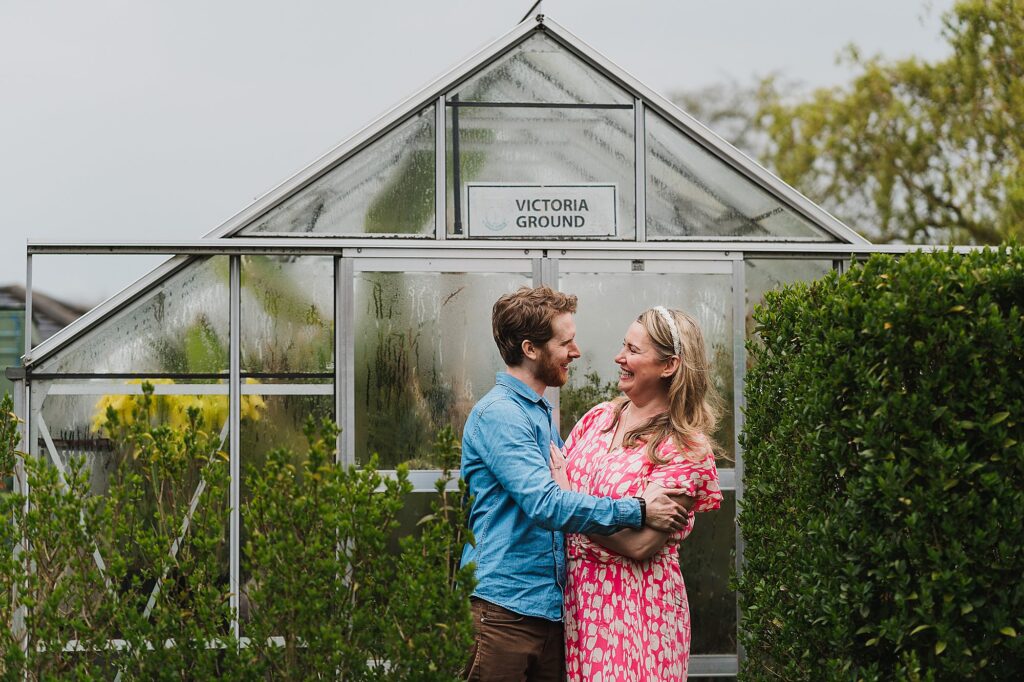 Bride and Groom to be giggling between themselves cuddling in front of the greenhouse in the parents garden //
Shropshire Wedding Photographer