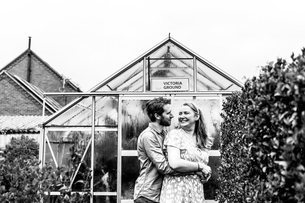 Black and white photo of bride and groom to be cuddling in the garden in front of the greenhouse // Charlotte Giddings Photography