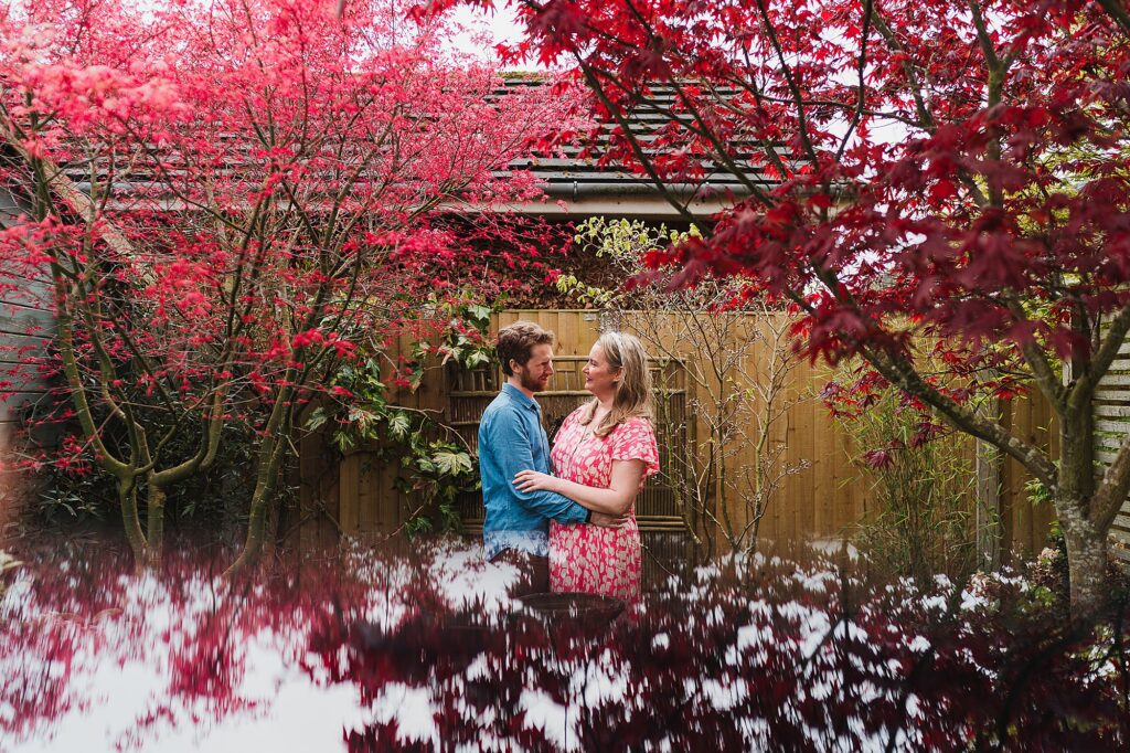 Bride and Groom to be looking at one another with a beautiful red backgrop of an acer tree // Charlotte Giddings Photography