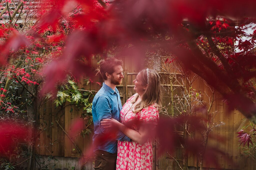 Bride and Groom to be chatting amongst a red acer tree in the garden on a pre wedding shoot
