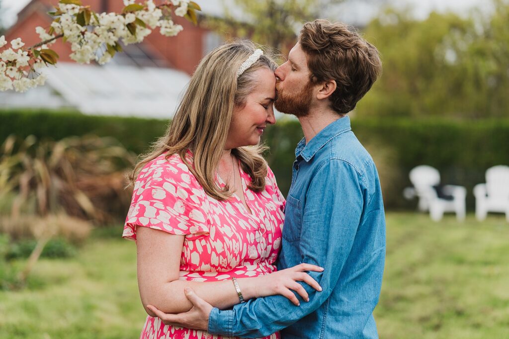 Groom to be kissing his bride to be on the forehead as they have a moment together in the garden in Shropshire