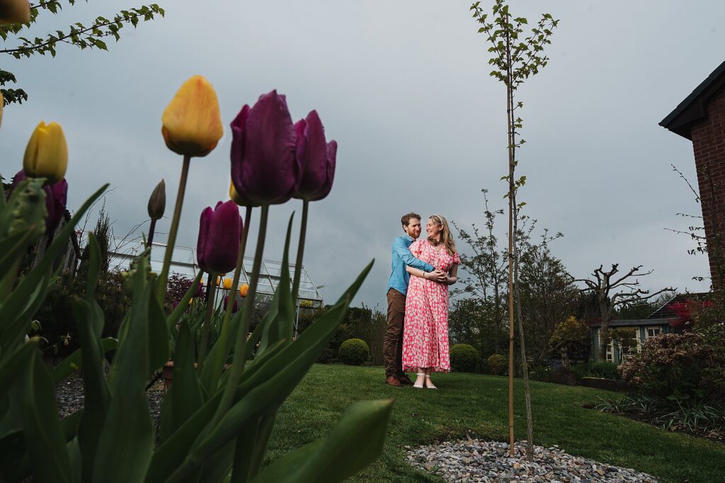 Bride and Groom to be cuddling in the garden with yellow and purple tulips in the garden // Charlotte Giddings Photography