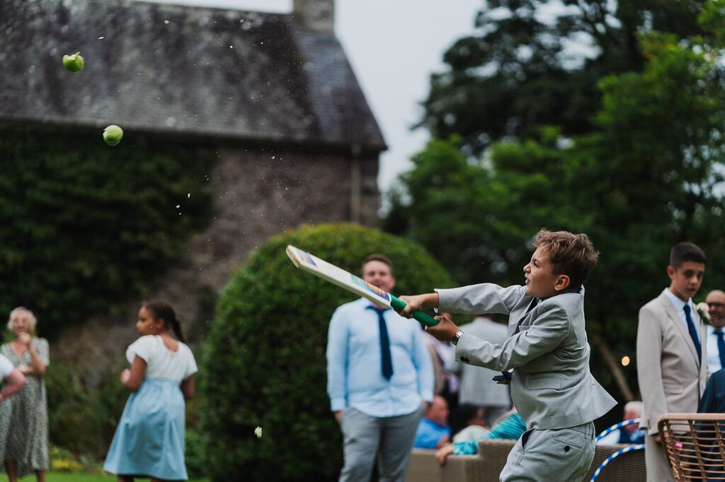 Young boy hitting apples to entertain themselves at a wedding in the gardens // Charlotte Giddings Photography