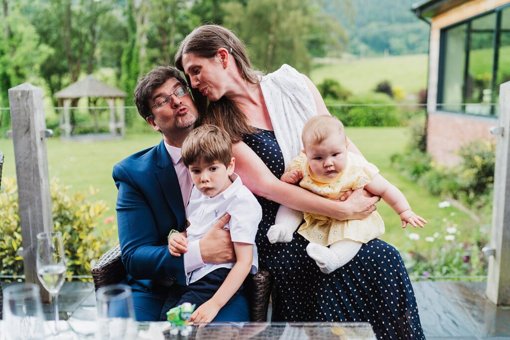Mum and dad attempting to kiss one another at a wedding holding their children at Tyn Dwr Hall // Tyn Dwr Hall wedding photographer