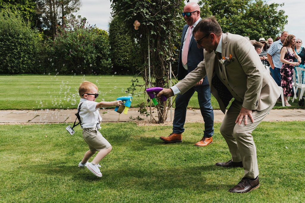 Page Boy and Father of the Groom having a play fight with bubble guns // Shropshire Wedding Photographer