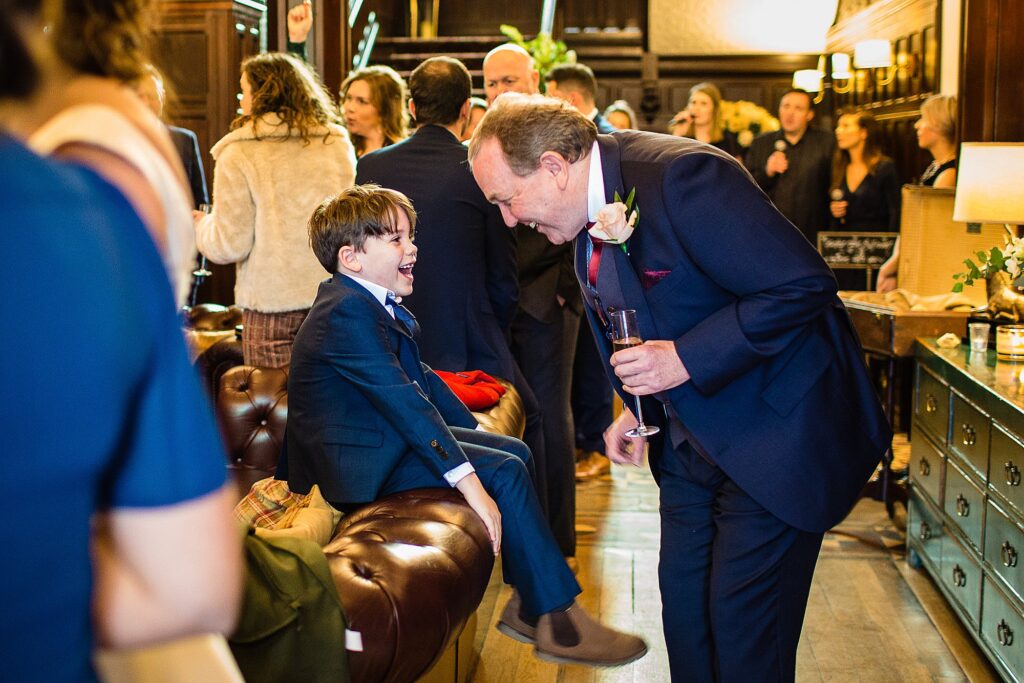 Little boy sat on the back of the sofa chatting away with an elderly guest giggling away // Tyn Dwr Hall Wedding Photographer