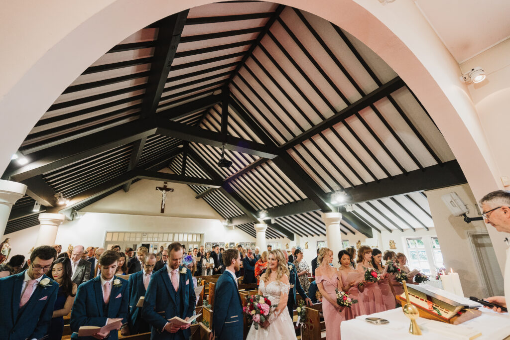 Bride and Groom looking at one another during their wedding ceremony at the Catholic church in Nantwich Cheshire with all the guests in the background // Cheshire Wedding Photographer