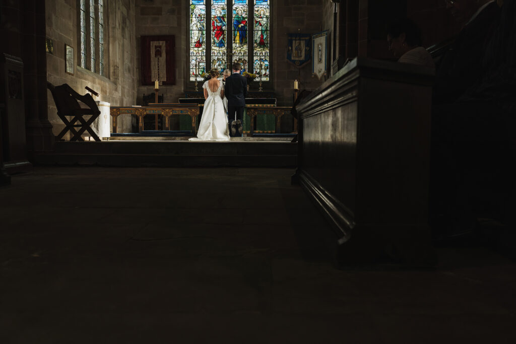 Bride and Groom at the top of the aisle in beautiful sunshine in Hanmer Church, Hanmer, Wales with a stunning backdrop of the stained glass window // Waled Wedding Photographer