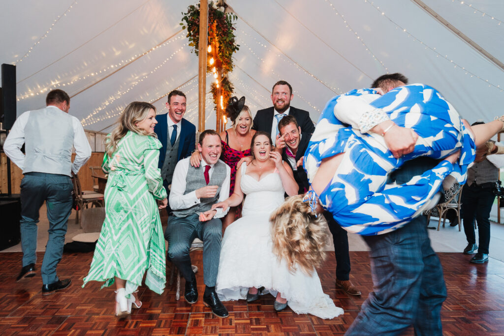 Bride and Groom partaking in the new trend of table dash and a couple come past running holding a lady in the air giggling // Wedding Photographer Shropshire