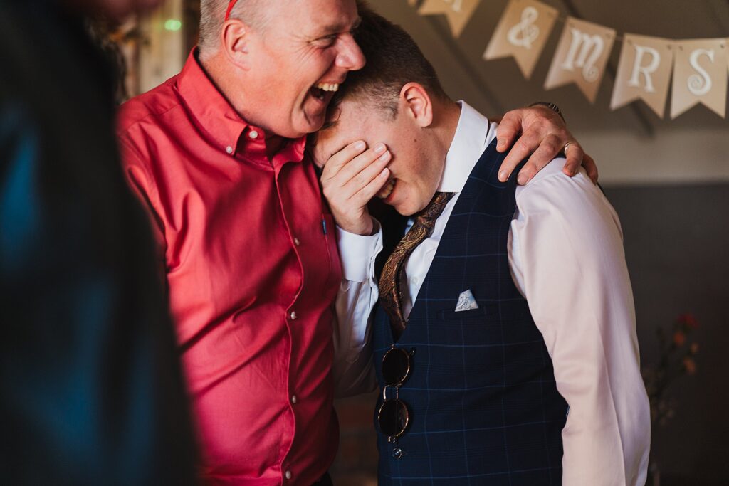 Wedding guests giggling and hugging a wedding guest holding his teary eyes at a micro wedding in Manchester // Wedding Photographer Manchester