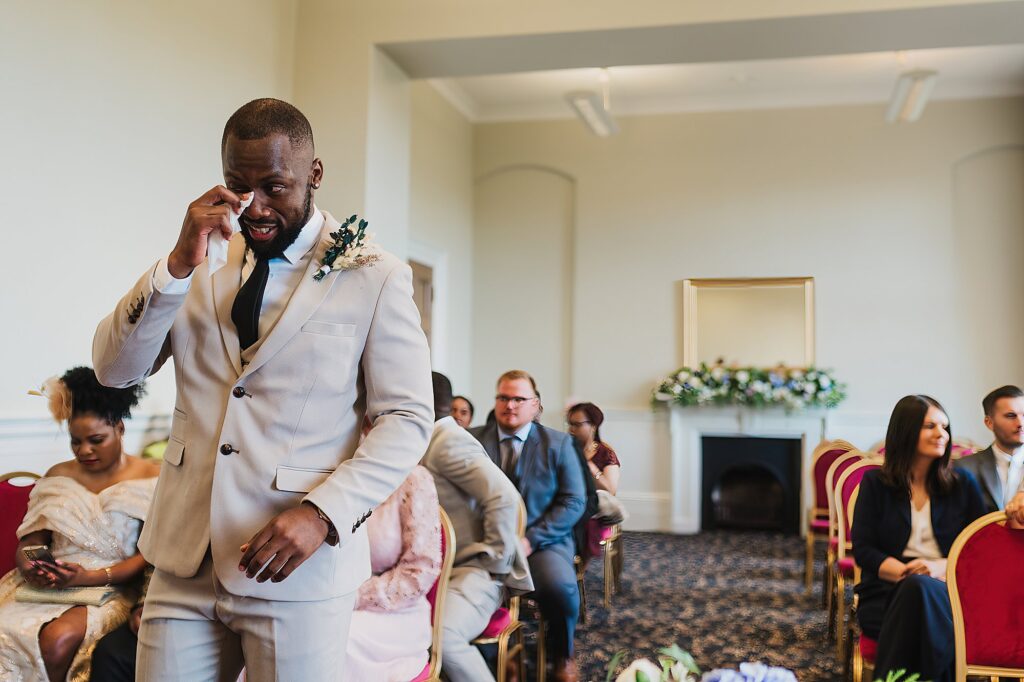 Groom wiping away tears at the top of the aisle waiting for his bride at St. George's Hall, Liverpool
