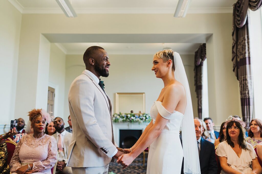 Bride and Groom beaming with smiles as they look at each other holding hands during the ceremony at St. George's Hall, Liverpool
