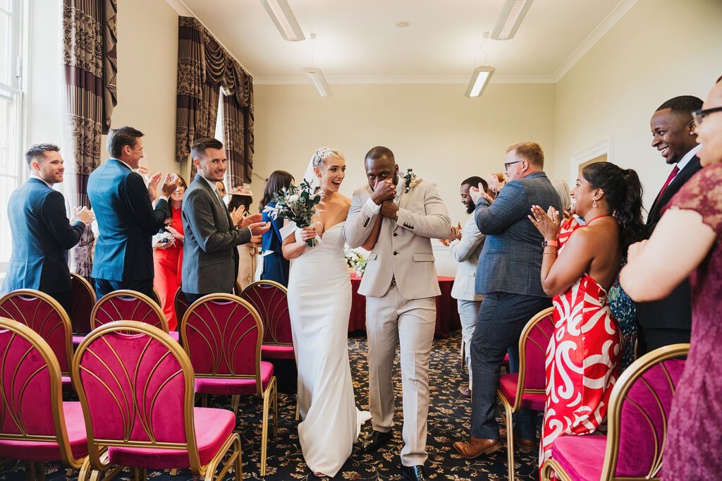 Groom kissing the bride's hand as they walk down the aisle as a happy married couple at St George's Hall

