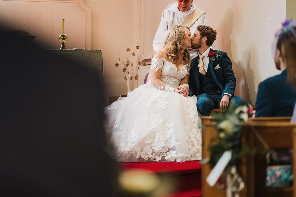Bride and Groom having a kiss at the top of the aisle and while the father is saying a verse from the bible // Shropshire Wedding Photographer