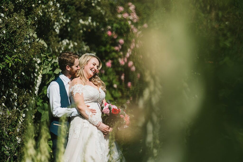 Bride and Groom giggling between themselves in the walled gardens and stunning roses at Combermere Abbey