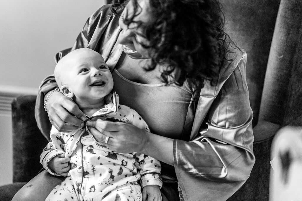 Bride's baby boy looking at one of the bridesmaid with a big smile as she changes him ready for the wedding // Grange Barn Winter Wedding Photographer