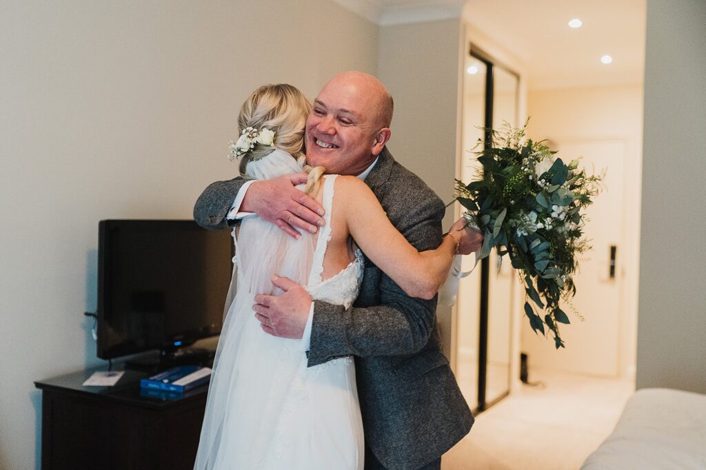 Father of the bride giving the bride a massive squeeze when he sees her in her wedding dress at Hill Valley Hotel, Whitchurch Shropshire