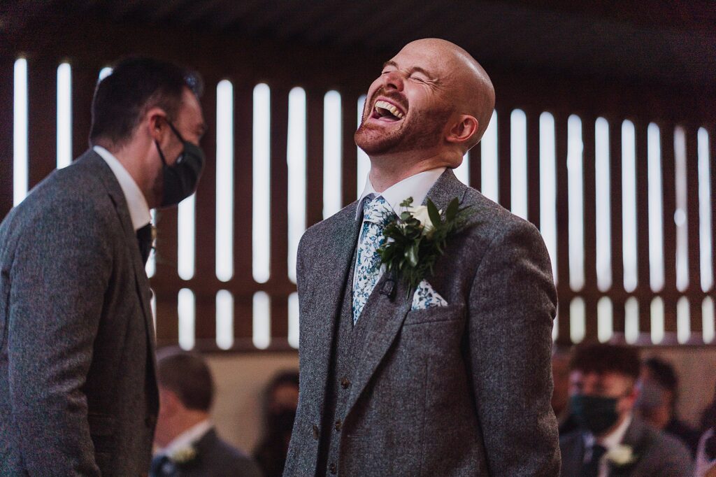Groom laughing out loud with his best man at the top of the aisle at Grange Barn Wedding Venue // Cheshire Wedding Photographer