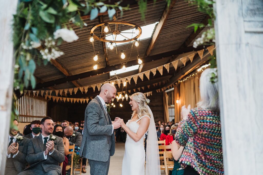 Bride and groom clutching hands and beaming with smiles looking at each other at the top of the aisle // Grange Barn Winter Wedding