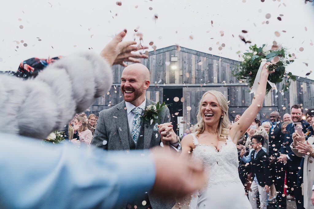 Bride and groom covered in confetti as people throw it at them at Grange Barn // Charlotte Giddings Photography