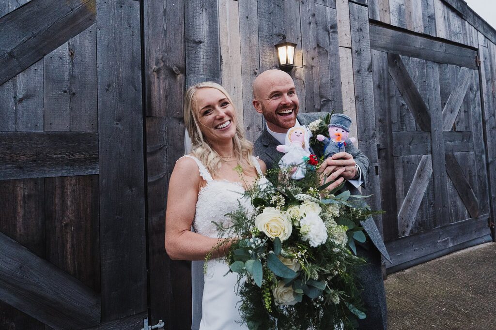 Bride and groom posing with knitted gifts from a wedding guest // Grange Barn Wedding