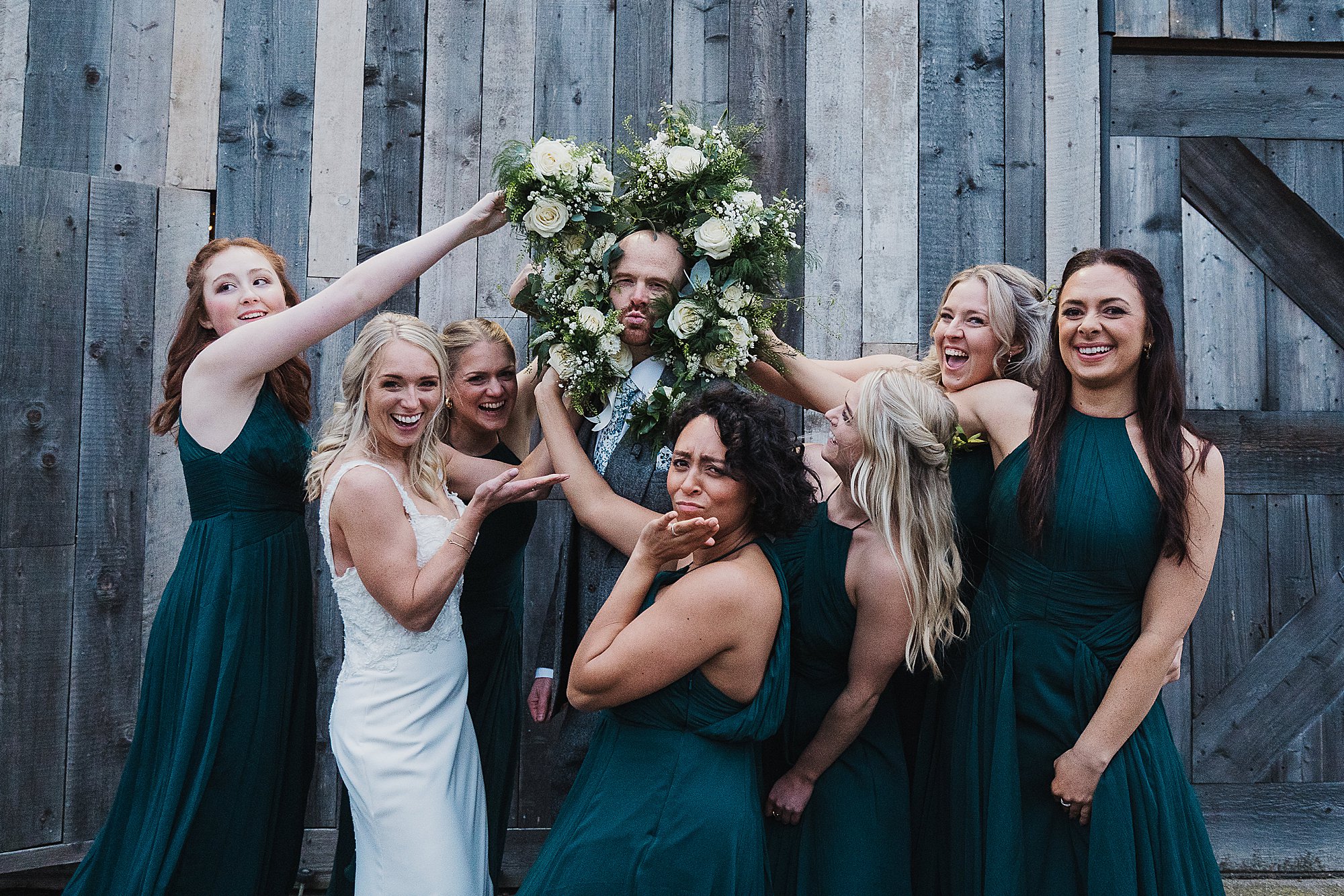 Cheshire Wedding Venue Grange Barn00039 Bride and the bridesmaid putting their bouquets around the groom's face like a lions mane //Grange Barn Wedding Photographer