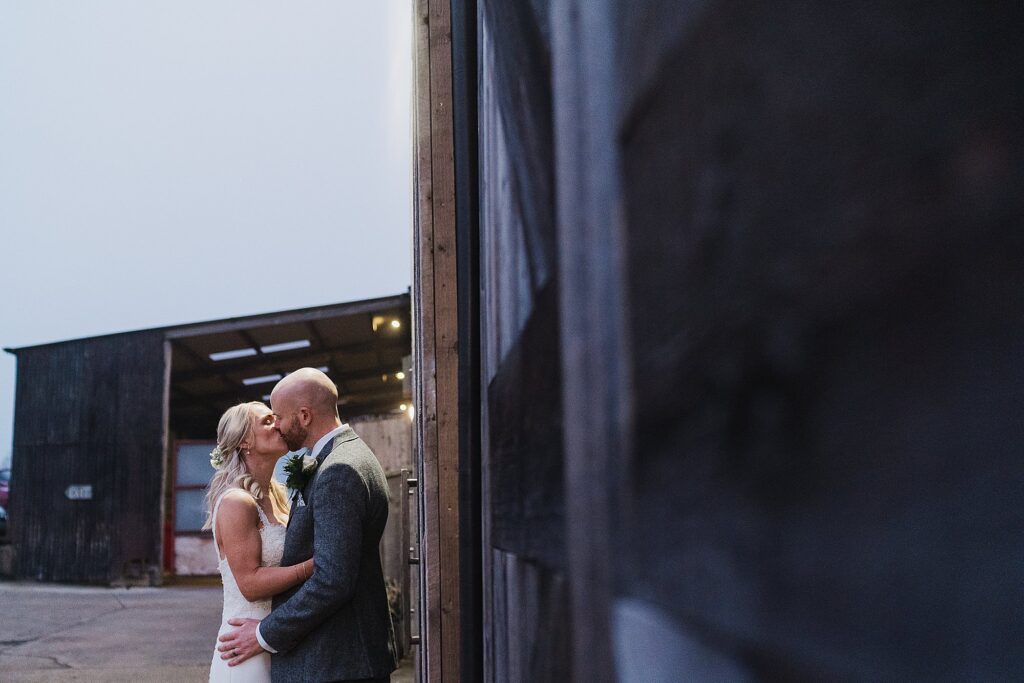 Bride and Groom kissing outside up against the large barn doors at Grange Barn Wedding Venue // Cheshire Wedding Photography