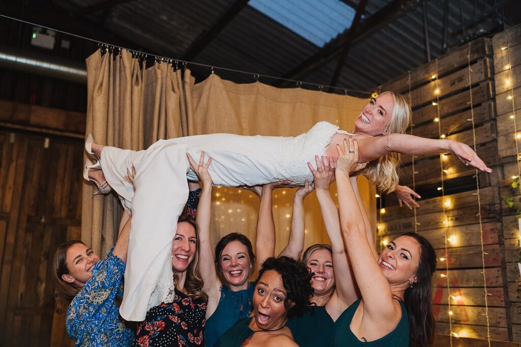 Bride being lifted up by her cheerleading girlfriends at Grange barn wedding photography