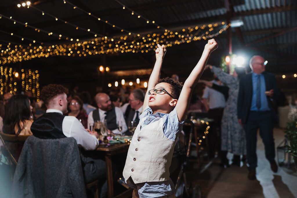 Little boy fist punching the air as the DJ starts up for the evening reception at Grange Barn Wedding Venue // Charlotte Giddings Photography