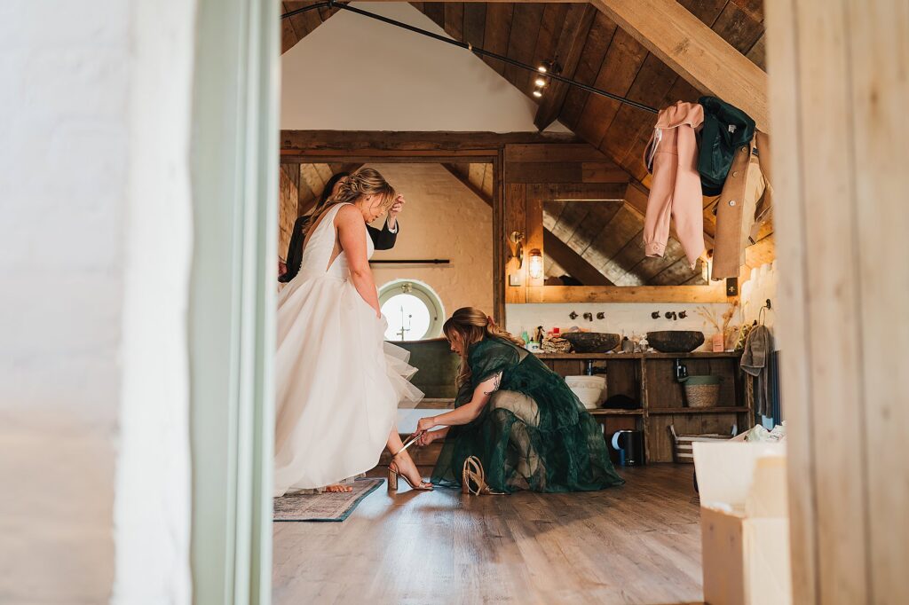 Bride ready in her dress while her sister is securing her wedding shoes for her // Charlotte Giddings Photography