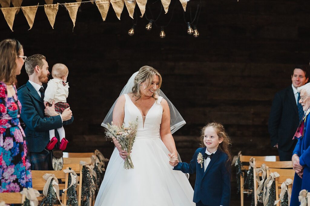 Bride being escorted down the aisle by her nephew at Grange Barn // Wedding Photographer Cheshire