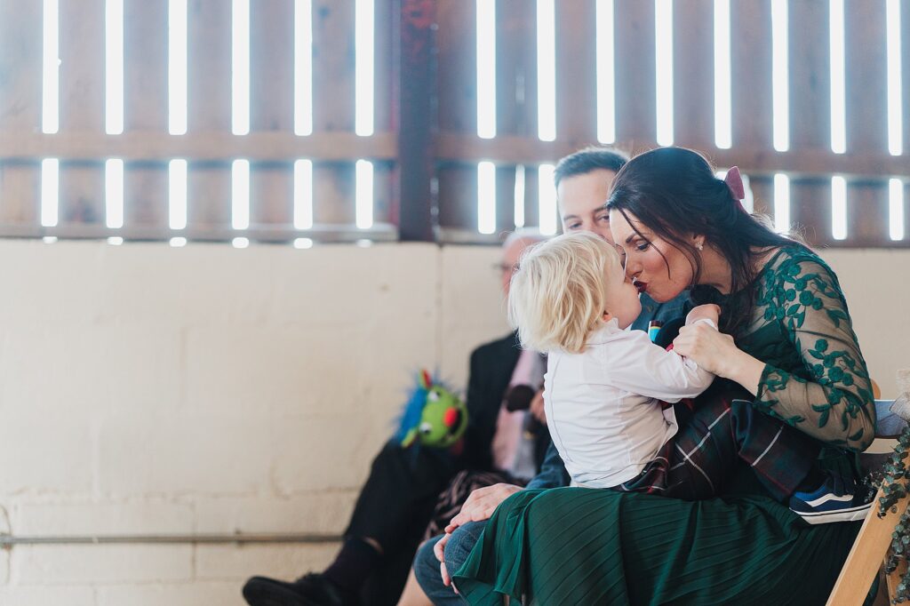 Bridesmaid sitting her little boy on her knee and giving him a little kiss on the lips before the wedding ceremony commences // Grange Barn Wedding Photography