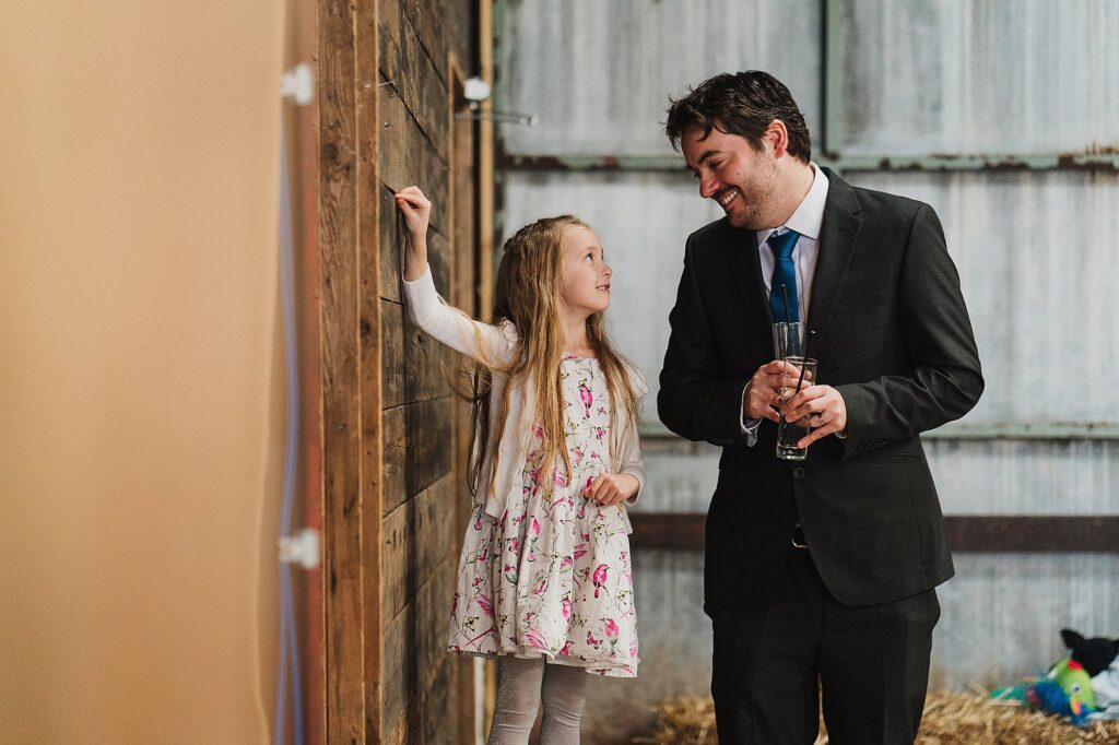 Little girl standing on a hay bale and looking up to her daddy who is standing next to her // Grange Barn Wedding Photographer