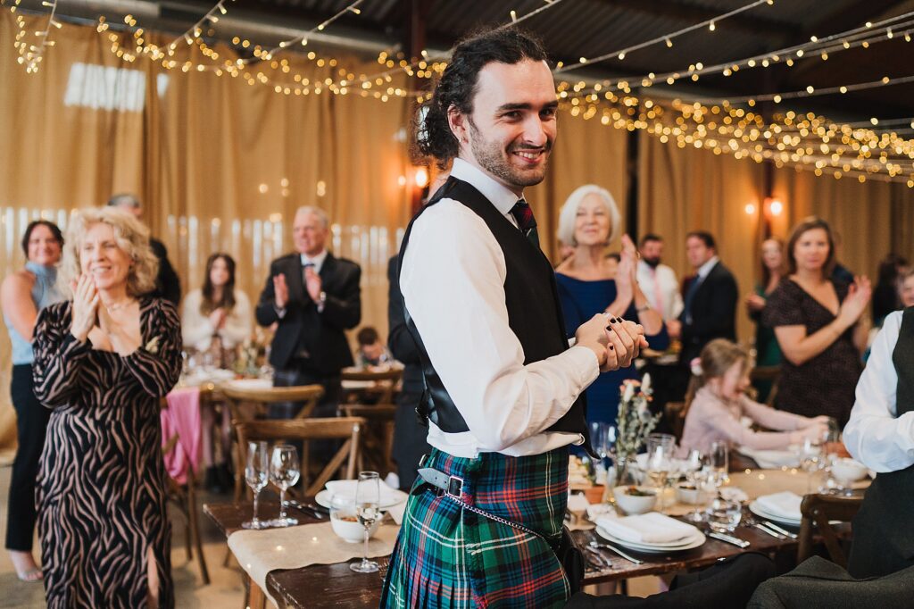 Guests standing up applauding their bride and groom as they walk into the wedding breakfast at Cheshire Wedding Venue Grange Barn