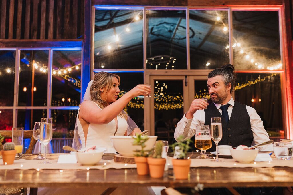 Bride and Groom picking up a shot glass each - one vodka and one water, they have no idea who has which at this point, a polish tradition // Grange Barn Wedding Venue