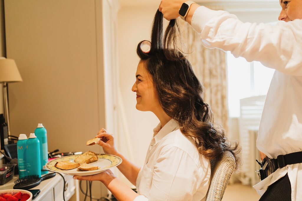 Bride eating toast giggling while she is having her hair and makeup done at Hencote Estate, Shrewsbury, Shropshire